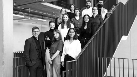 Gruppe von Architekt:innen und Mitarbeitenden, die gemeinsam auf einer Treppe in einem modernen Bürogebäude stehen.