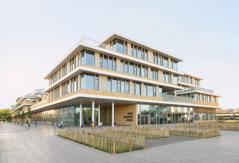 „Außenansicht des mehrgeschossigen Holz- und Glasgebäudes der Josef Schwarz Schule mit terrassierten Ebenen und einem großen überdachten Eingangsbereich.“