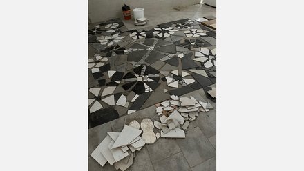 Innenraum im Umbau: am Boden liegen in Stern- und Fächerformen ausgelegte Bruchfliesen in Grau, Schwarz und Weiß; daneben Haufen ungenutzter Stücke und ein Eimer.