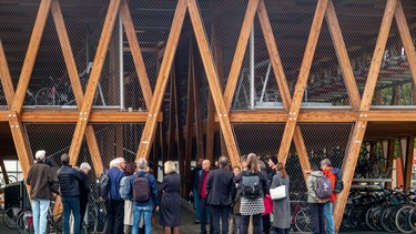 Außenansicht einer Fahrradgarage; davorstehende Personengruppe betrachtet das Gebäude