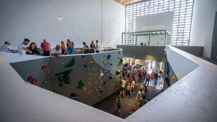 Umgenutzte Kirche als Boulderhalle: große, helle Halle mit farbigen Klettergriffen an Wänden; Besucherinnen und Besucher klettern oder schauen zu, Licht fällt durch ein großes Glasbausteinfenster.
