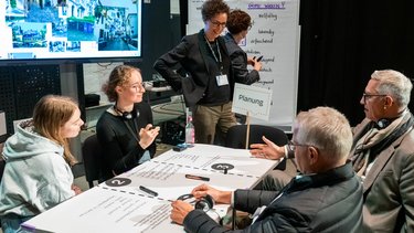 Workshoprunde mit Diskussionstisch Teilnehmende erarbeiten gemeinsam Inhalte an einem moderierten Tisch.