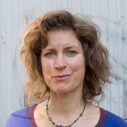 Porträt einer Frau mit lockigem Haar vor einer hellen Wand im Außenbereich.