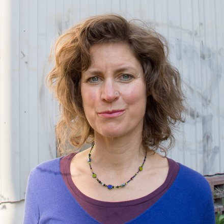 Porträt einer Frau mit lockigem Haar vor einer hellen Wand im Außenbereich.