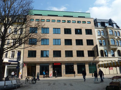 Moderner Geschäftsbau mit heller Natursteinfassade und REWE im Erdgeschoss
