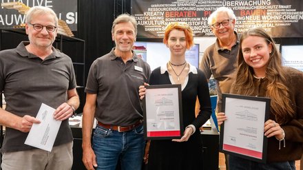 Mehrere Personen zeigen Urkunden und Anerkennungen auf einem Messestand.