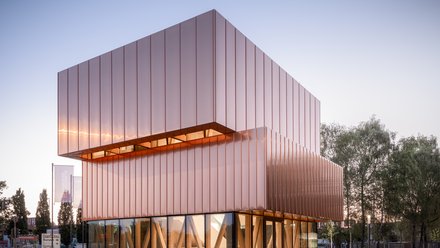 Kubischer Pavillon mit kupferfarbener Metallfassade und vollständig verglastem Erdgeschoss.