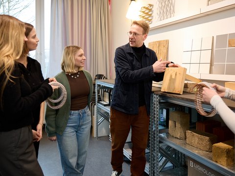 „Ein Dozent erklärt einer Gruppe von Studentinnen verschiedene nachhaltige Holz- und Baustoffproben in einem Materialarchiv.“