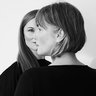 "Schwarzweiß-Porträtfoto zweier Frauen von hinten, überlagert in doppelter Belichtung. Beide haben schulterlange Haare mit Pony. Eine Frau schaut nach links, die andere nach rechts. Beide tragen dunkle Kleidung vor neutralem, hellem Hintergrund."
