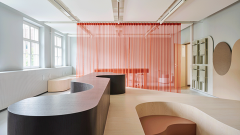 Moderner Innenraum mit geschwungener Empfangstheke, integrierter Sitzbank und halbtransparenten Vorhängen. Große Fenster sorgen für viel Tageslicht und eine helle, offene Atmosphäre.