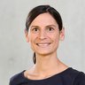 Ein Porträt zeigt eine einzelne erwachsene Person vor neutralem Hintergrund, frontal zur Kamera ausgerichtet und ruhig lächelnd, wodurch das Bild eine professionelle Darstellung vermittelt und für Autorenschaft, fachliche Kompetenz oder eine persönliche Stimme innerhalb eines kulturellen oder fachlichen Kontextes steht.