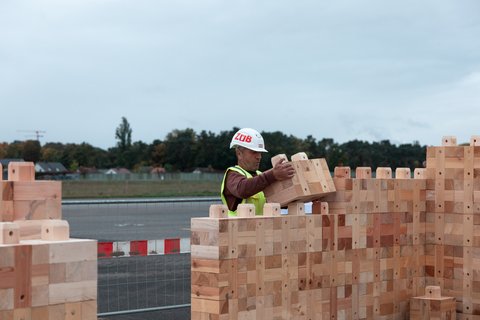 Bauarbeiter setzt Holzbausteine zu einer Wand zusammen.