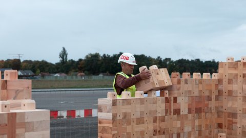 Bauarbeiter setzt Holzbausteine zu einer Wand zusammen.