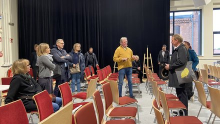 Gruppe von Teilnehmenden bei einer Führung in einem Saal mit roten Stuhlreihen.