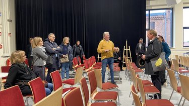 Gruppe von Teilnehmenden bei einer Führung in einem Saal mit roten Stuhlreihen.