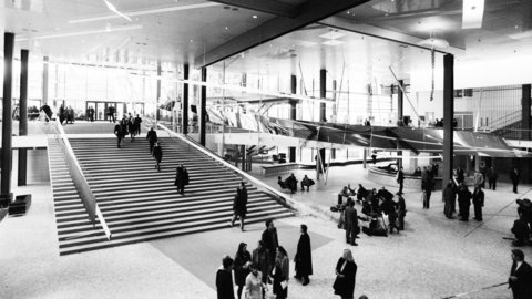 Großer heller Innenraum mit breiter Treppe, mehreren Personen und moderner Architektur mit Glaswänden