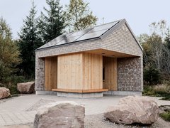 Kleines Gebäude mit Holzverkleidung und Schindeldach in natürlicher Umgebung mit großen Steinen davor