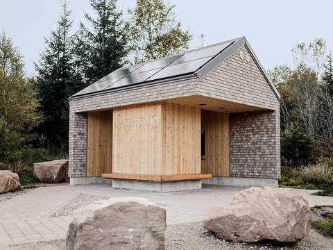 Kleines Gebäude mit Holzverkleidung und Schindeldach in natürlicher Umgebung mit großen Steinen davor