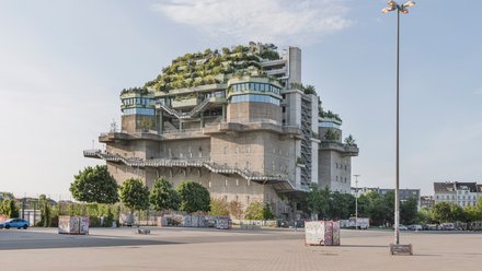 Massiver Betonbunker mit terrassenförmiger Begrünung und öffentlich zugänglichen Ebenen.