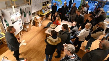 Menschen hören einer Präsentation zu und betrachten Ausstellungstafeln im Raum der IBA’27.