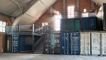 Umgenutzte Industriehalle mit gestapelten Schiffscontainern, die zu Räumen mit Treppe und Terrasse ausgebaut wurden.