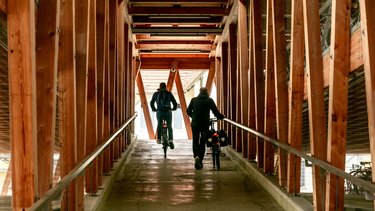 Innenansicht eines Fahrradparkhauses; zwei Personen verlassen das Fahrradparkhaus mit ihren Fahrrädern auf der Rampe 