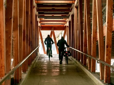 Innenansicht eines Fahrradparkhauses; zwei Personen verlassen das Fahrradparkhaus mit ihren Fahrrädern auf der Rampe 