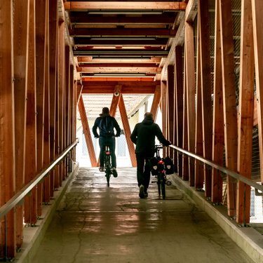 Innenansicht eines Fahrradparkhauses; zwei Personen verlassen das Fahrradparkhaus mit ihren Fahrrädern auf der Rampe 