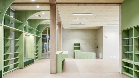 Leerer Raum mit grünen Regalen und Theken aus Holz sowie sichtbaren Betonstützen und -wänden
