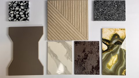 Sammlung verschiedener Materialmuster auf Weiß: Terrazzo, gerilltes Holz, dunkler Kunststein, braunes Formteil, Platte in Marmoroptik, patinierte Oberfläche, harzartiges Gesteinsmuster.