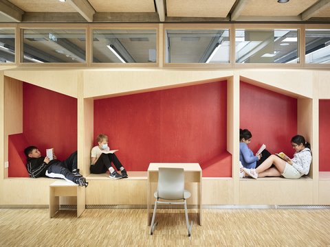 Vier Kinder sitzen in zwei Nischen mit roten Wänden und lesen, davor steht ein Tisch mit einem Stuhl