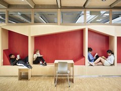 Vier Kinder sitzen in zwei Nischen mit roten Wänden und lesen, davor steht ein Tisch mit einem Stuhl