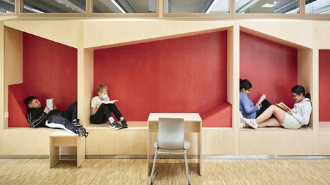 Vier Kinder sitzen in zwei Nischen mit roten Wänden und lesen, davor steht ein Tisch mit einem Stuhl