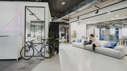 Moderner Büro- und Aufenthaltsbereich mit Sofa, Glasräumen, Fahrrad und Personen in Bewegung.