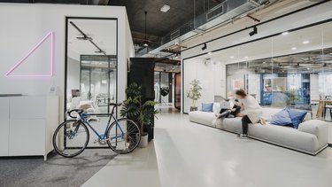 Moderner Büro- und Aufenthaltsbereich mit Sofa, Glasräumen, Fahrrad und Personen in Bewegung.