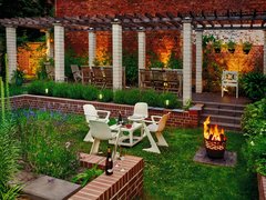 Gemütlicher, beleuchteter Garten mit Sitzgruppe, Feuerkorb und Pergola vor Backsteinwand.