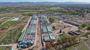 Luftaufnahme von zwei parallel angeordneten Hallen in einer ländlichen Siedlungslandschaft. 