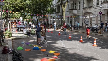 Autofreie Spielstrasse mit Passanten und Kindern, die auf der Straße spielen.