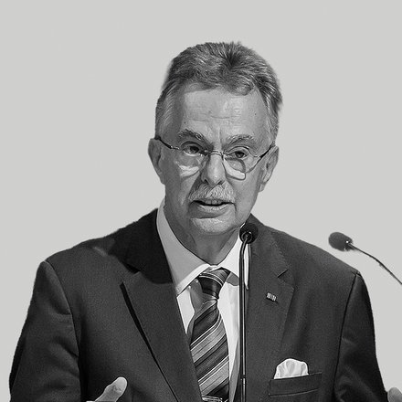 Schwarzweißfoto eines älteren Mannes in formeller Kleidung (Sakko, Krawatte, Einstecktuch) mit Brille und Schnurrbart, der gestikulierend an einem Rednerpult in ein Mikrofon spricht; auf dem Pult ist die Aufschrift „Architektenkammer Nordrhein‑Westfalen“ zu sehen.