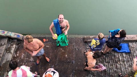 Mehrere Menschen stehen nach dem Schwimmen an einer Uferkante eines Kanals, trocknen sich ab oder ziehen sich um. Die Aufnahme zeigt die Szene von oben.