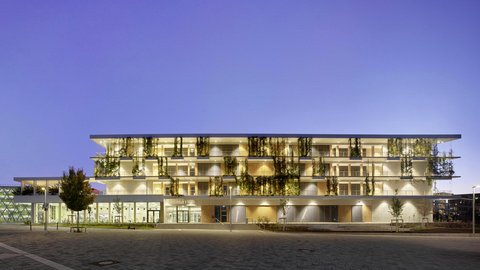Modernes mehrstöckiges Schulgebäude mit großen Fenstern und begrünten Balkonen bei Dämmerung