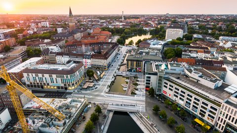 Luftaufnahme des neu gestalteten Holstenfleets in Kiel mit Wasserflächen, Fußgängerbereichen und umliegender Innenstadt; im Hintergrund ist die Kieler Stadtsilhouette zu sehen.
