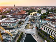 Luftaufnahme des neu gestalteten Holstenfleets in Kiel mit Wasserflächen, Fußgängerbereichen und umliegender Innenstadt; im Hintergrund ist die Kieler Stadtsilhouette zu sehen.