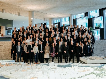 Großes Gruppenfoto von Teilnehmenden auf einer Treppe in einem modernen Gebäude, im Vordergrund ein Stadtmodell.