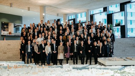 Großes Gruppenfoto von Teilnehmenden auf einer Treppe in einem modernen Gebäude, im Vordergrund ein Stadtmodell.