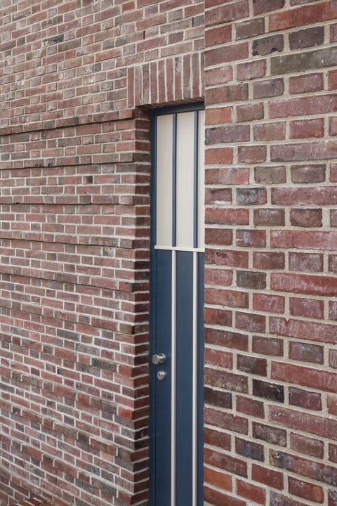 Detail einer schmalen, bodentiefen Fensteröffnung in einer Backsteinfassade.