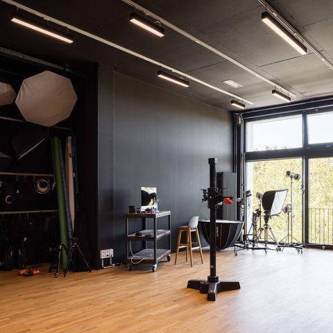 Fotostudio mit schwarzer Wand, Holzfußboden, Beleuchtungsausrüstung, Stuhl und großem Fenster mit Blick ins Freie