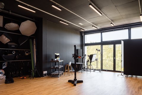 Fotostudio mit schwarzer Wand, Holzfußboden, Beleuchtungsausrüstung, Stuhl und großem Fenster mit Blick ins Freie