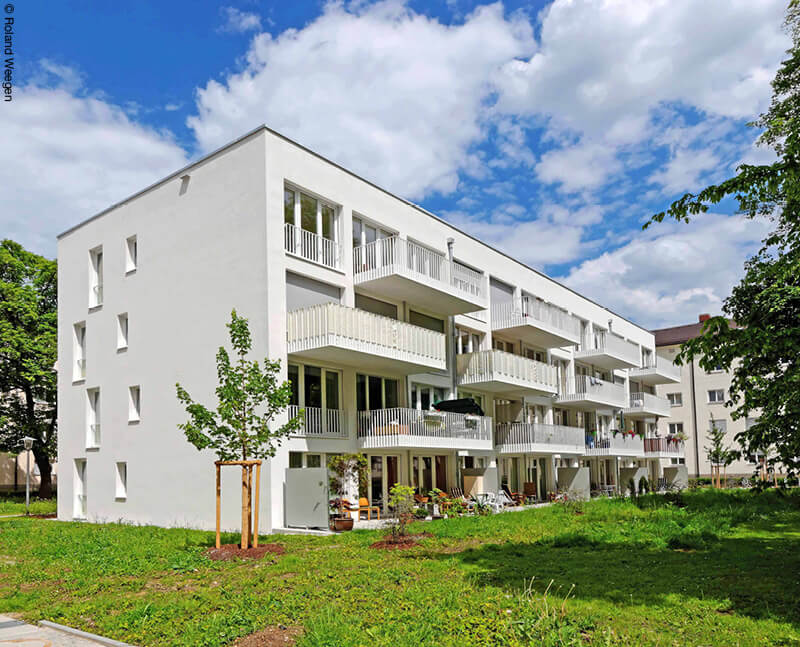 Weißes Wohnhaus mit großen Balkonen auf grüner Wiese