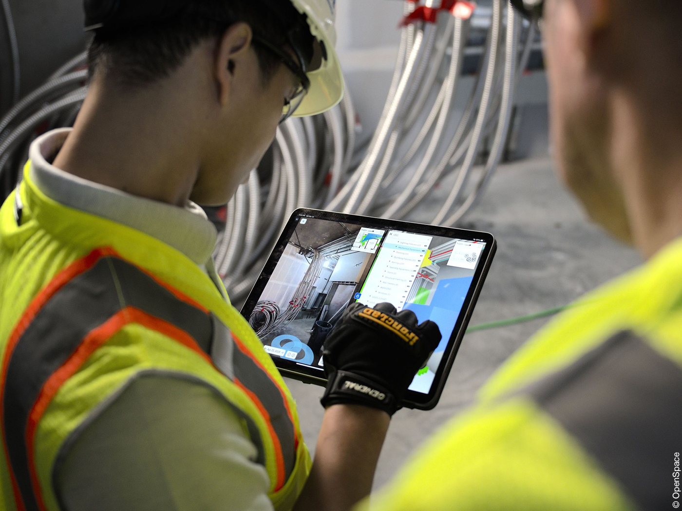 Zwei Baustellen-Arbeiter schauen auf den Bildschirm eines Tablets und begutachten die virtuelle Version ihrer Baustelle.